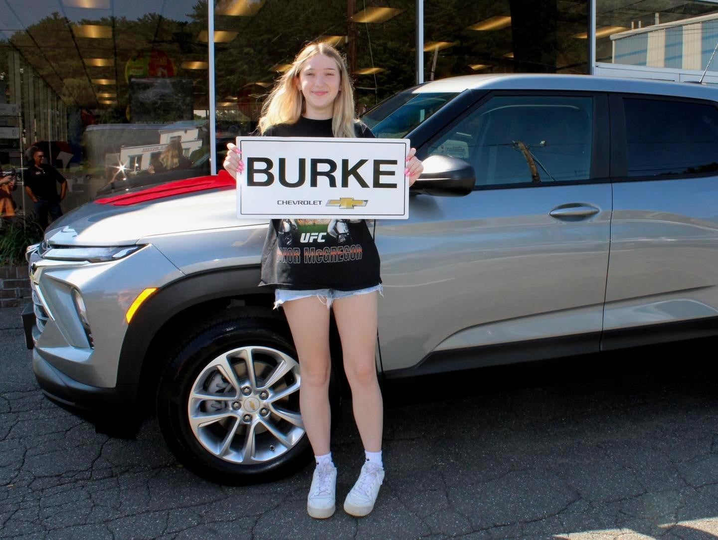 Younger_girl_customer_holding-small-copy-burke-chevrolet-with_standing_beside_a_vehicle